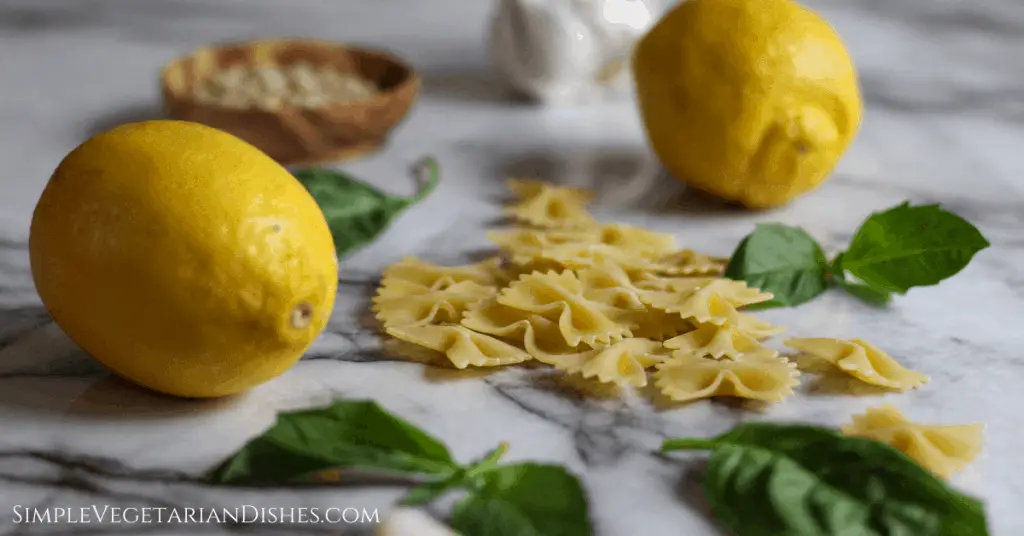 lemon pepper pasta ingredients on marble table, including pine nuts, garlic, and basil