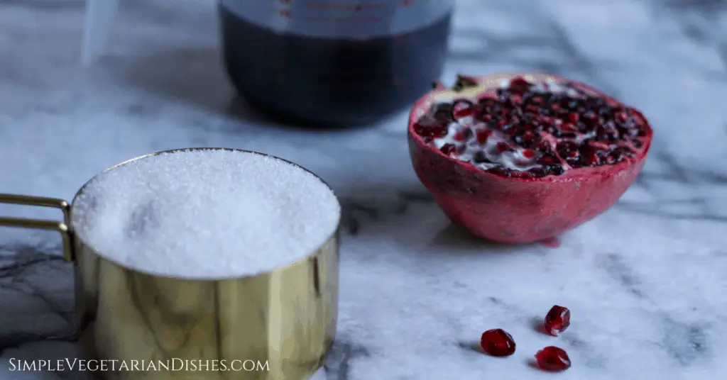 grenadine ingredients with half pomegranate and arils, sugar on marble table