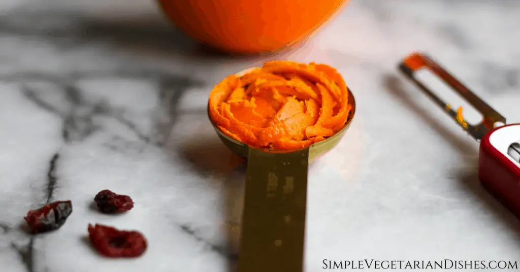 orange zest in gold measuring spoon on marble table with orange and cranberries 