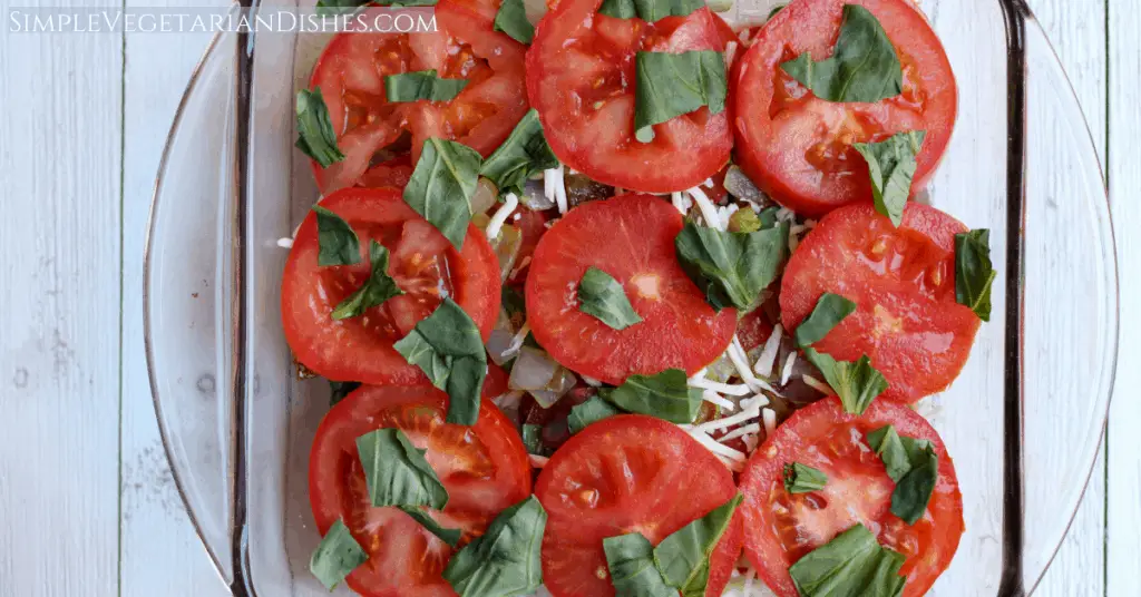 crustless tomato pie top layer with tomatoes, basil, cheese, and onions in baking dish