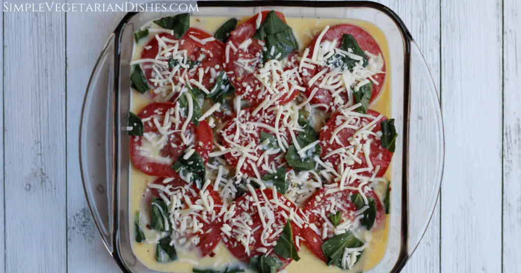 crustless tomato pie ready to bake with cheese on top in casserole dish on white board background