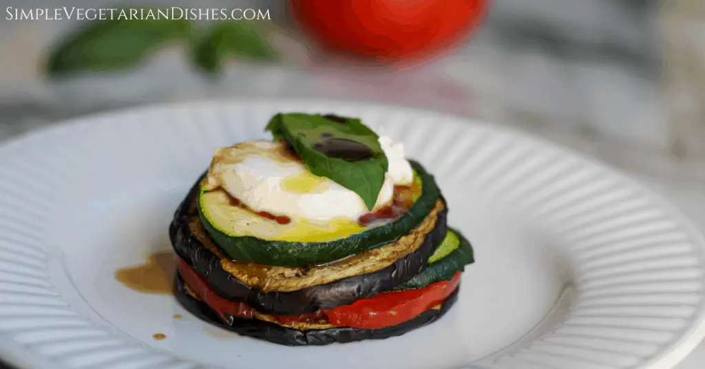 eggplant Napoleon on white plate with basil on top, drizzled with balsamic and EVOO