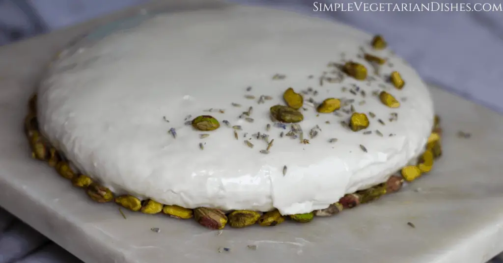 gateau vert green cake ready on marble cutting board garnished with lavender buds and pistachios