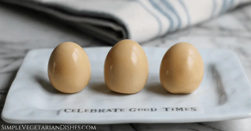 three hamine eggs peeled, revealing the whites of the eggs have turned brown