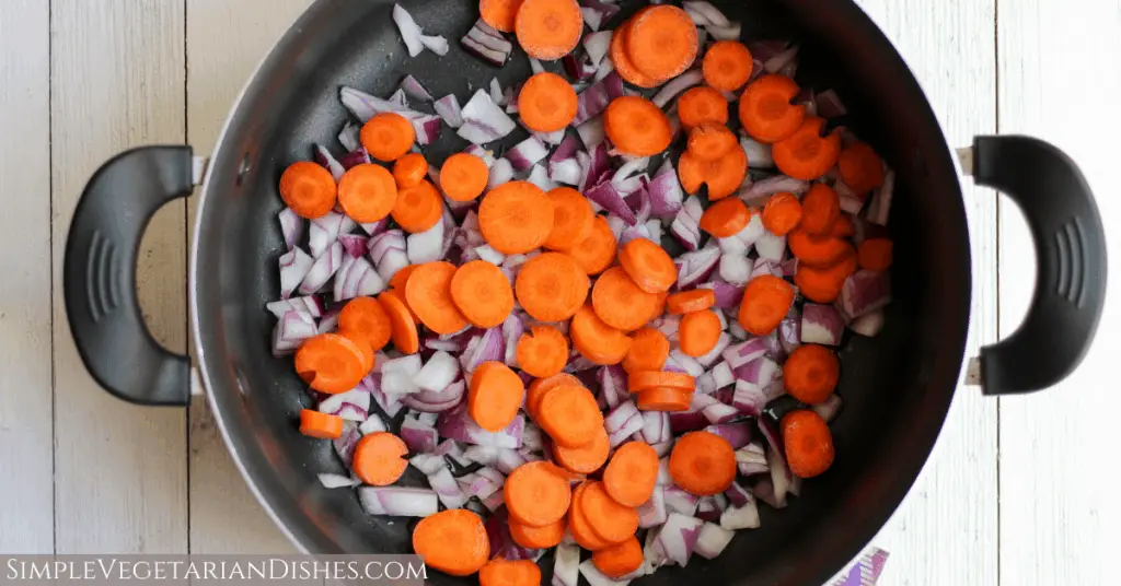 carrot rounds and diced red onion in dutch oven on white board background