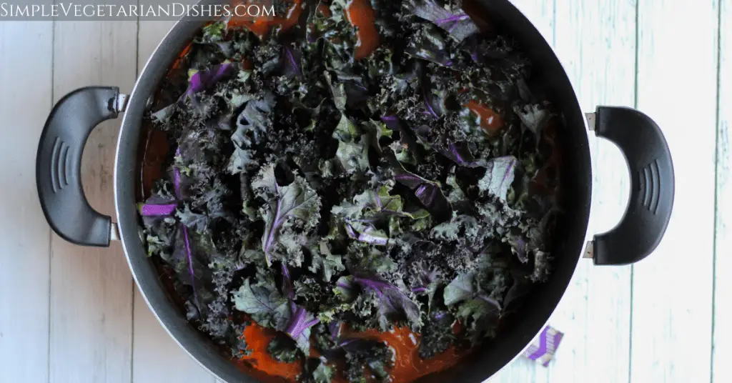 raw purple kale on top of soup in dutch oven on white boards