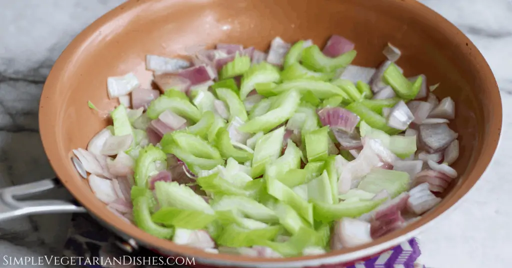 celery and red onion in copper skillet on white marble table with purple potholder