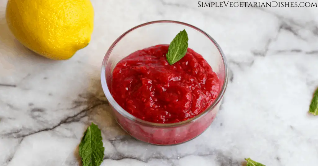 raspberry Melba sauce done in glass dish on marble table, garnished with fresh mint with lemon in background