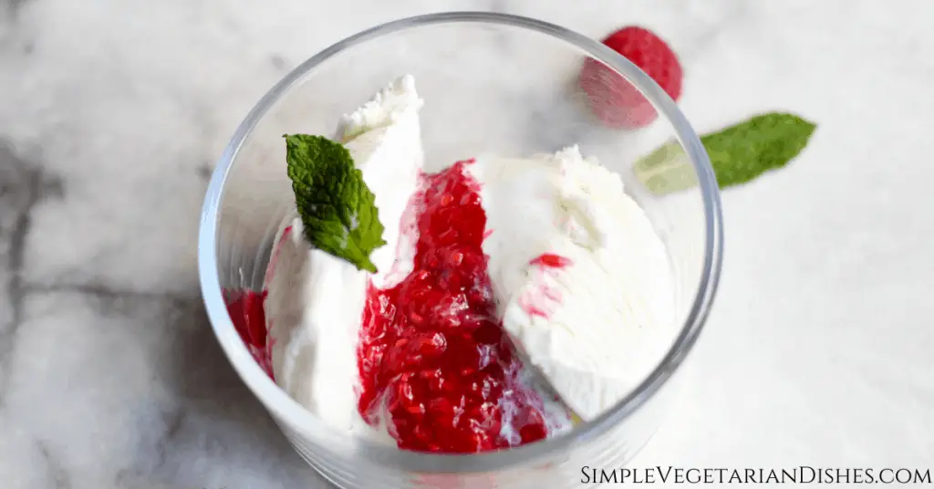 raspberry Melba sauce over vanilla ice cream in glass bowl, garnished with fresh mint on marble table