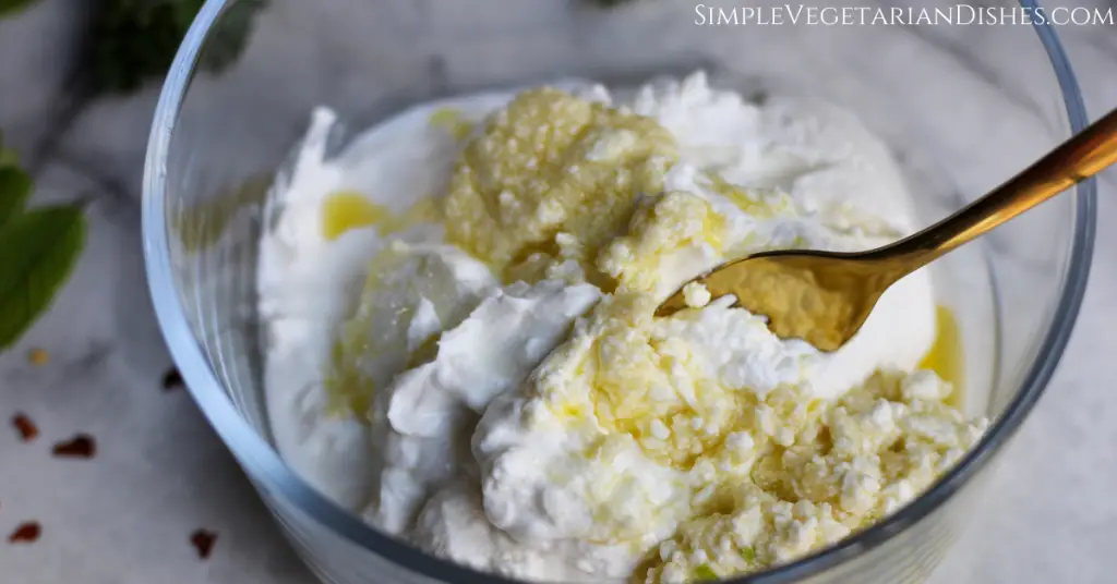 haydari flavoring poured over greek yogurt in glass bowl with gold fork