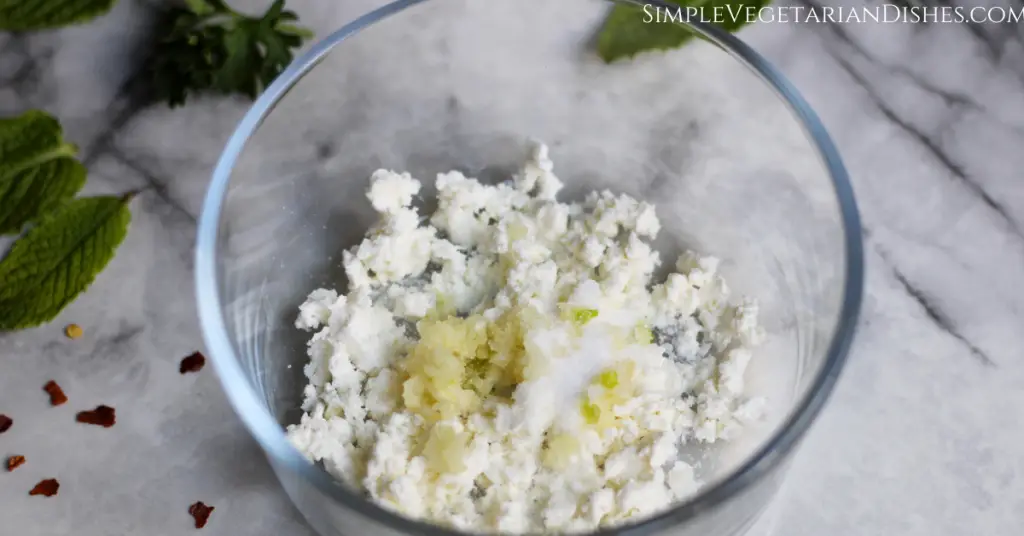 salt fresh minced garlic and feta crumbles in glass bowl with fresh mint leaves in background