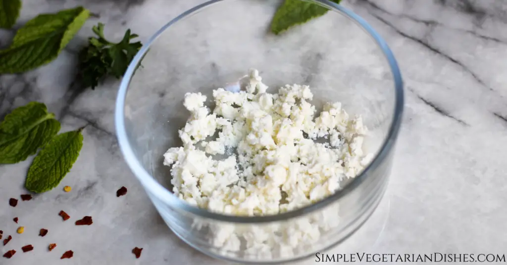 crumbled feta cheese in glass bowl with fresh mint in background