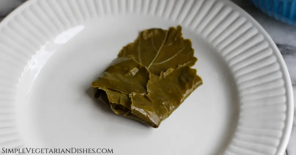 stuffed grape leaf folded like an envelope before rolling on white plate