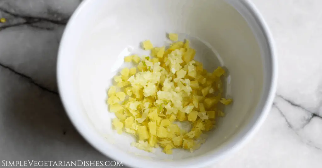 minced fresh ginger and garlic in white bowl on white marble table