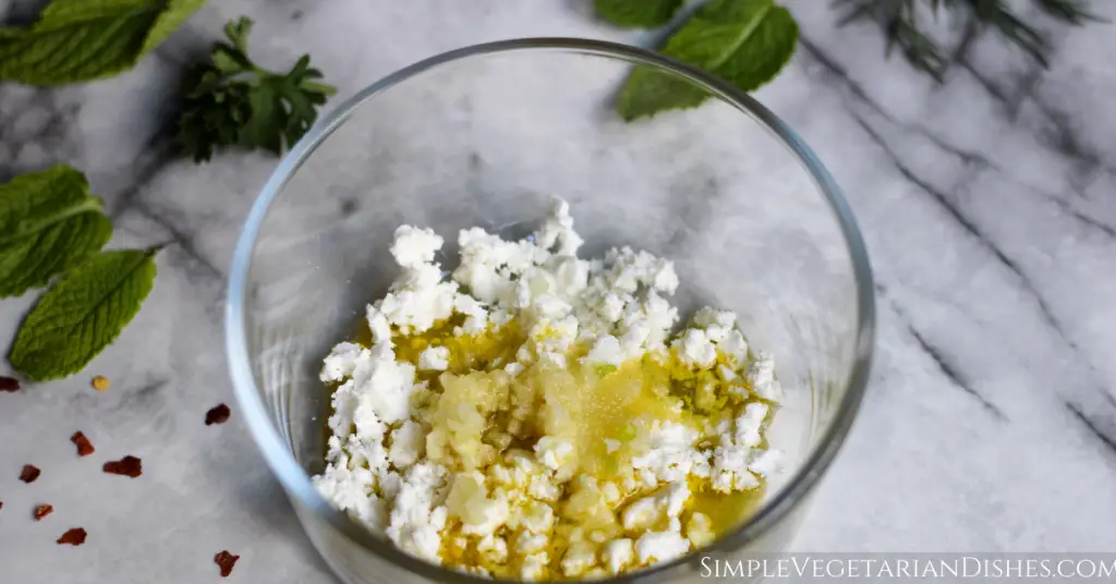 olive oil salt minced garlic and feta crumbles in glass bowl with mint in background