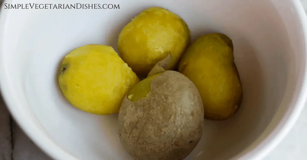 three peeled Yukon gold potatoes and one with peel hanging off in white mixing bowl