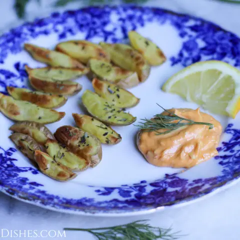 harissa aioli with roasted potato wedges served on blue china with lemon wedge on white marble table