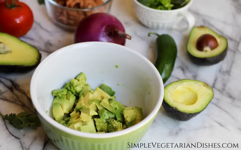 chunks of avocado in green bowl with ingredients in background