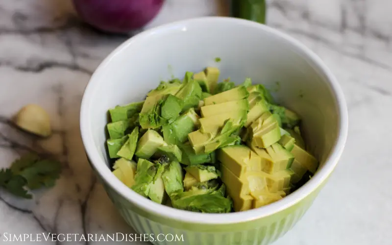 green mixing bowl full of avocado chunks on white marble table