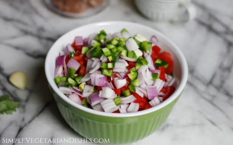 chopped jalapeno, onion, tomato and avocado in green mixing bowl