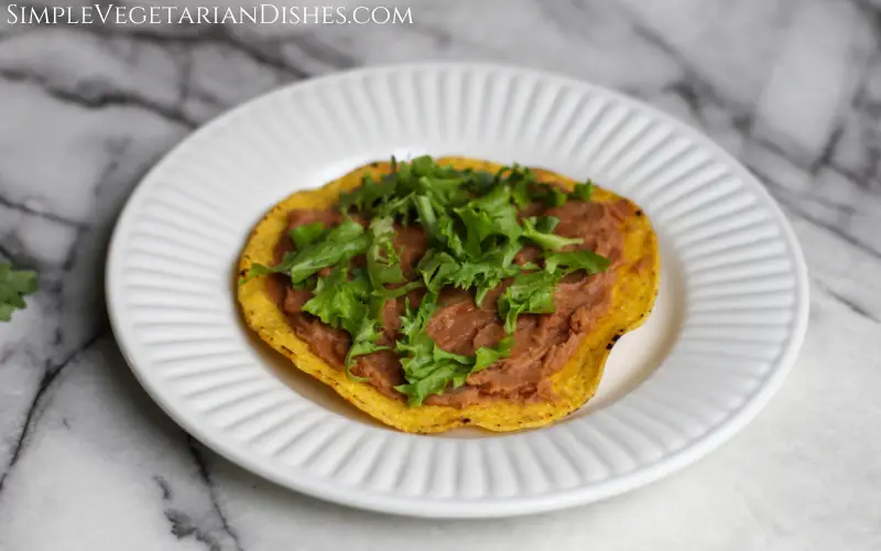 beginning layers of tostaguac on tostada shell on white plate