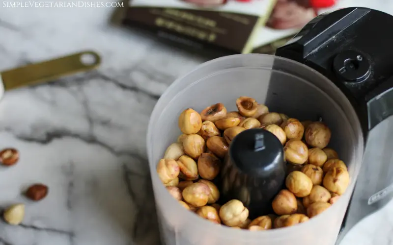 toasted hazelnuts for gianduja in black food processor on white marble table