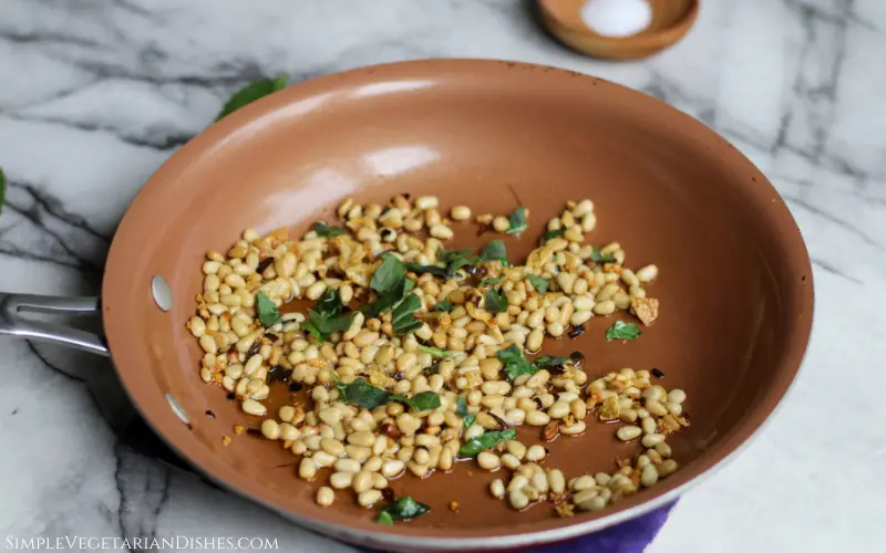 fresh basil, toasted pine nuts, and roasted garlic in copper skillet