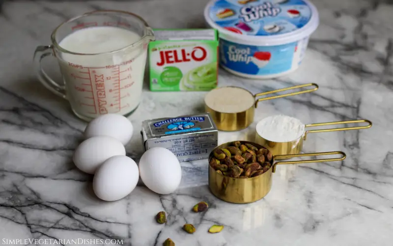 eggs, milk, butter, flour, sugar, cool whip, pistachios, pistachio pudding on white marble table