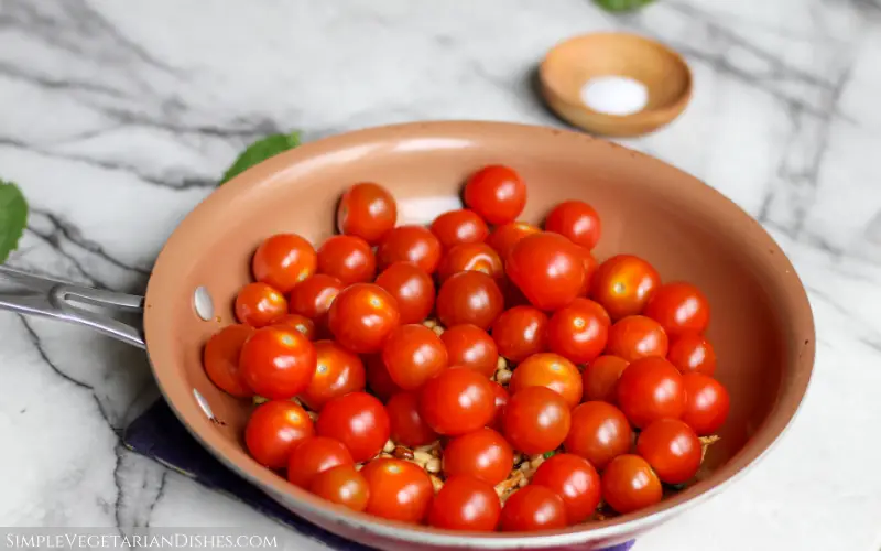 cherry tomatoes on top of pine nuts in copper skillet