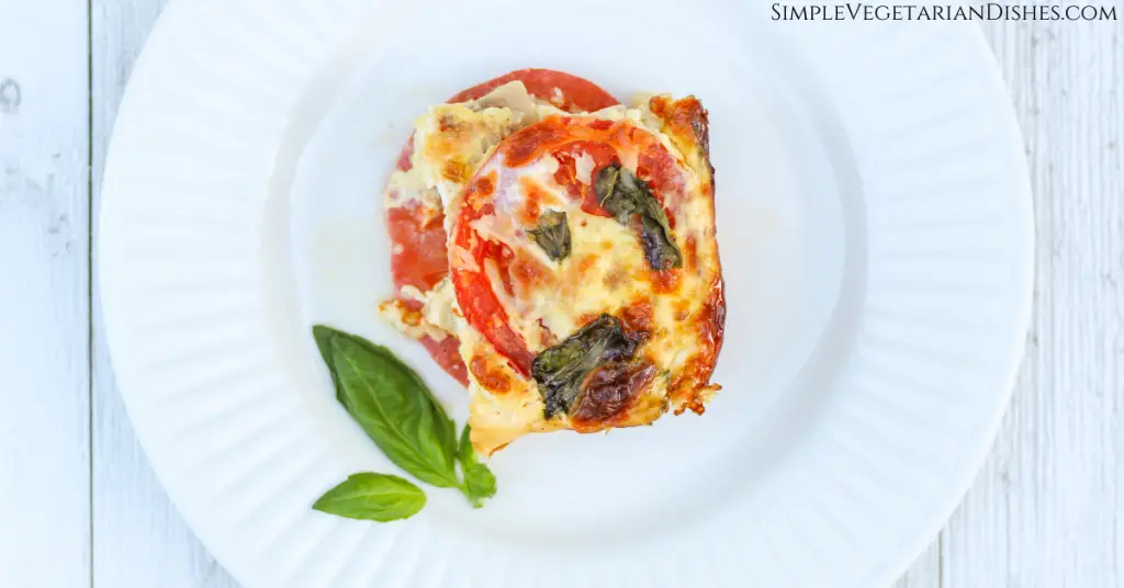 crustless tomato pie slice served on white plate on white board background garnished with fresh basil