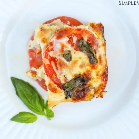 crustless tomato pie slice served on white plate on white board background garnished with fresh basil