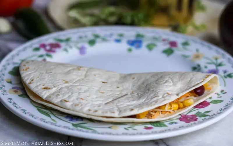 quesadilla ready to go in air fryer tortilla stuffed with cheese corn and beans held closed with toothpick on floral plate