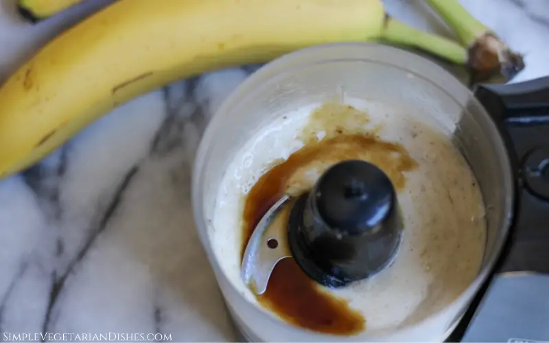 vanilla extract poured on blended frozen bananas in food processor