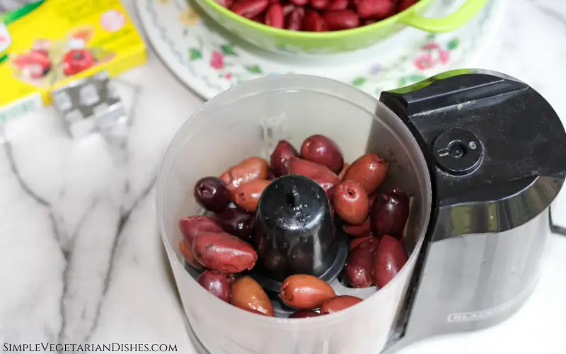 food processor full of pitted kalamata olives with kidney beans in background