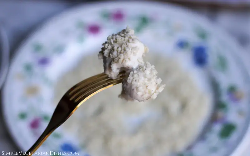 one breaded cauliflower wing held up on a golden fork