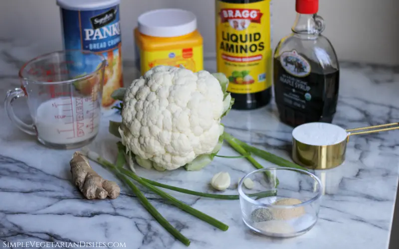 cauliflower, maple syrup, soy sauce, cornstarch, breadcrumbs, milk, ginger, green onions, garlic, spices, flour on white marble table