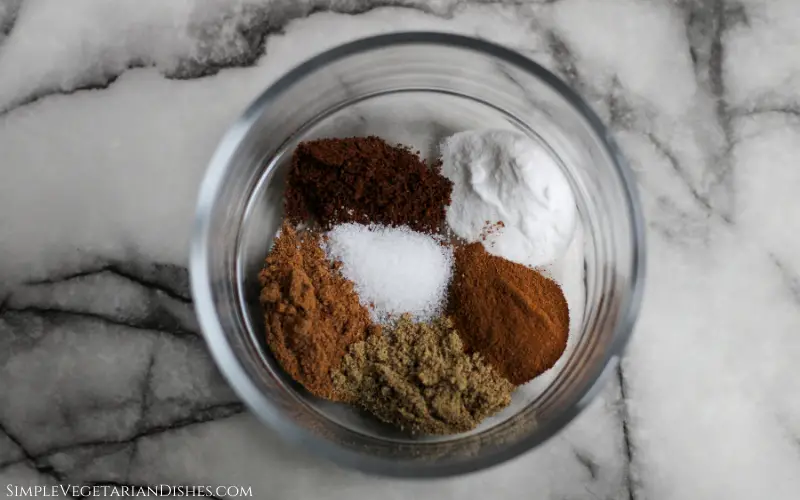cinnamon, nutmeg, cardamom, cloves, baking soda, and salt in glass bowl on white marble table