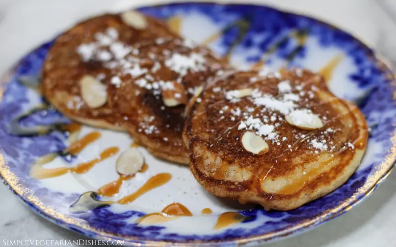three churro pancakes overlapping on blue china with powdered sugar and sliced almonds