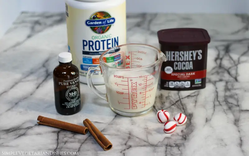 shake mix, cocoa, vanilla, almond milk, cinnamon sticks and peppermints on white marble table