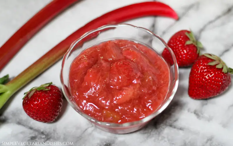 strawberry rhubarb sauce in small glass bowl with fruit in background