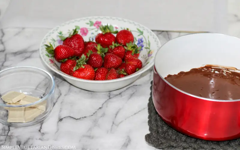 melted candy coating in red pan with bowl of berries