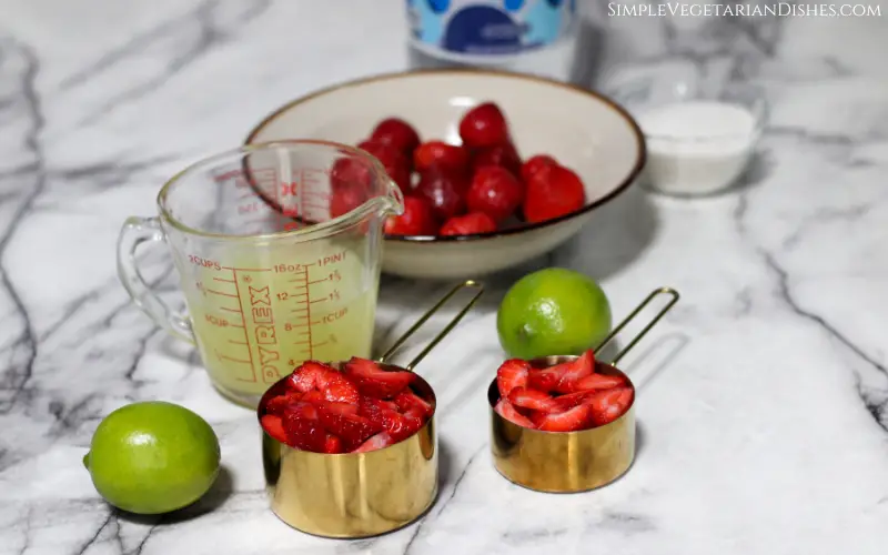 sliced strawberries in gold measuring cups with lime juice to make strawberry limeade