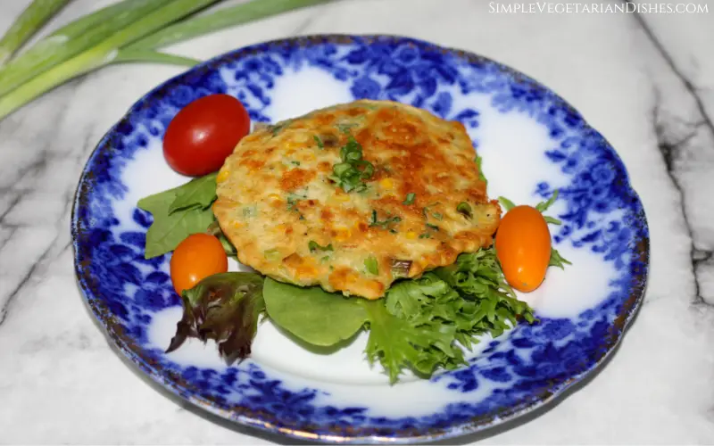 a gluten-free corn fritter served over lettuce garnished with green onion with cherry tomatoes on the side