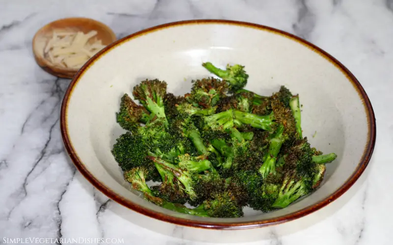 bowl of air fried broccoli with pinch bowl of parmesan cheese in background