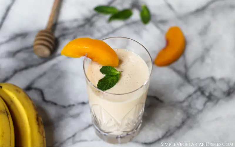 banana peach smoothie served in crystal glass with bananas in background