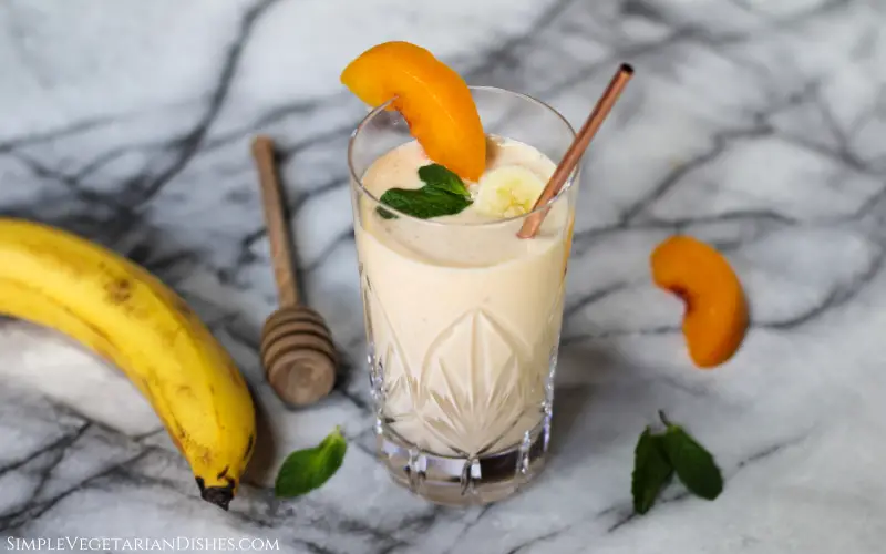 banana peach smoothie garnished with banana, peach and mint in crystal glass