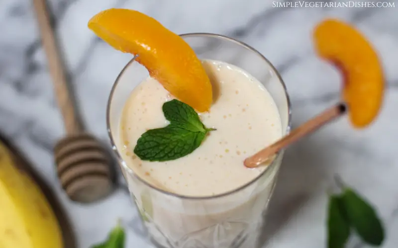 banana peach smoothie close up garnished with peach and mint
