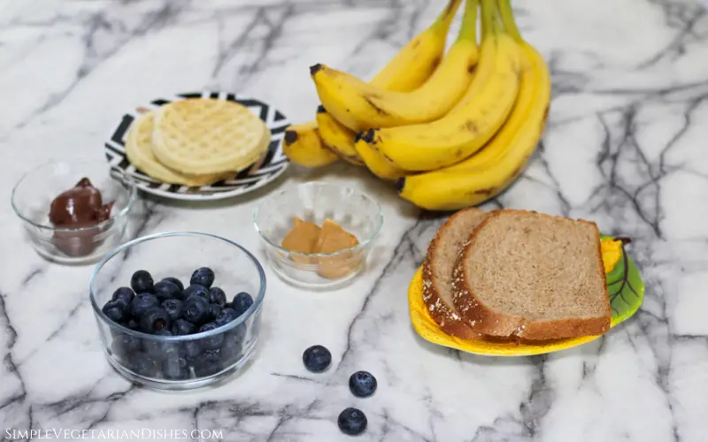 bread, waffles, bananas, blueberries, peanut butter and nutella on white marble table