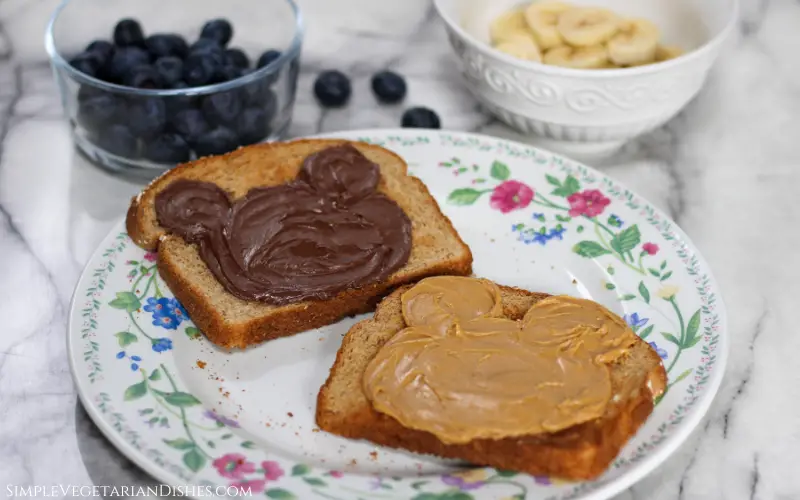 bread spread with peanut butter and nutella with fruit in background