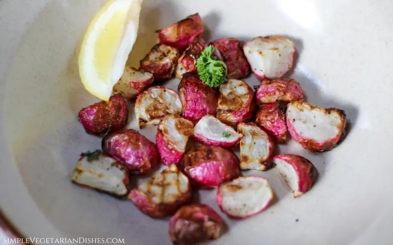 air fryer radishes in tan bowl with lemon wedge and parsley garnish